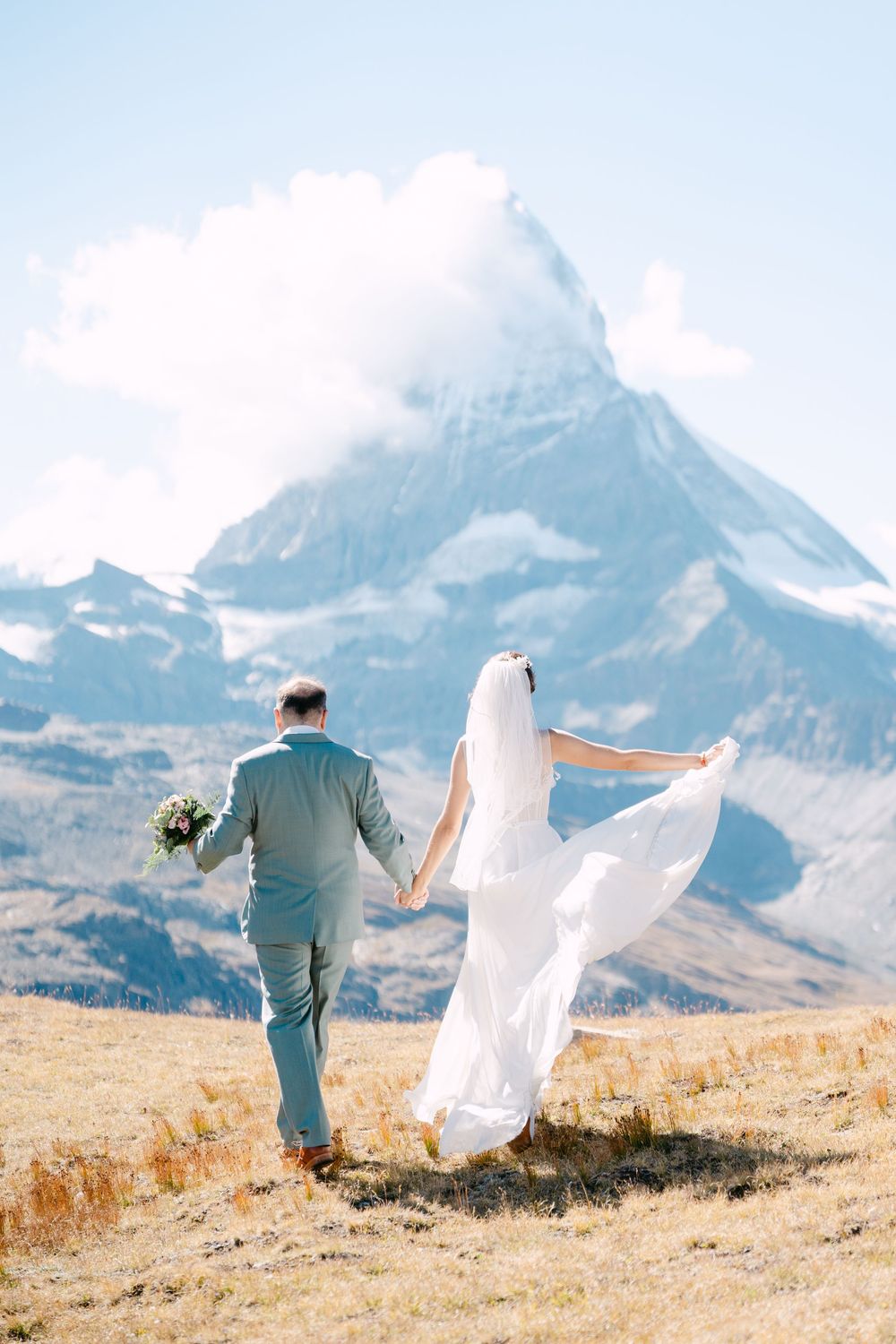 A couple dances joyfully on a mountainside meadow with dramatic snow-capped peaks in the background in Zermatt.