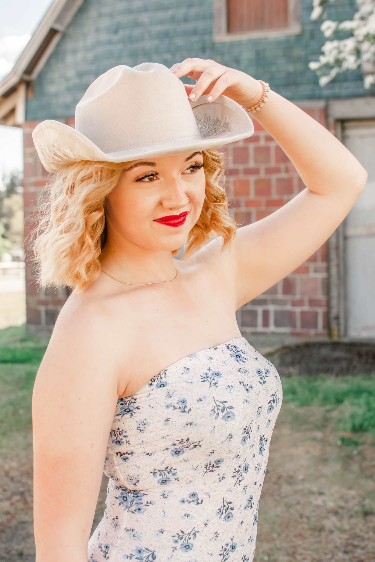 Stylish feminine portrait with white sunhat and floral dress against brick wall backdrop.
