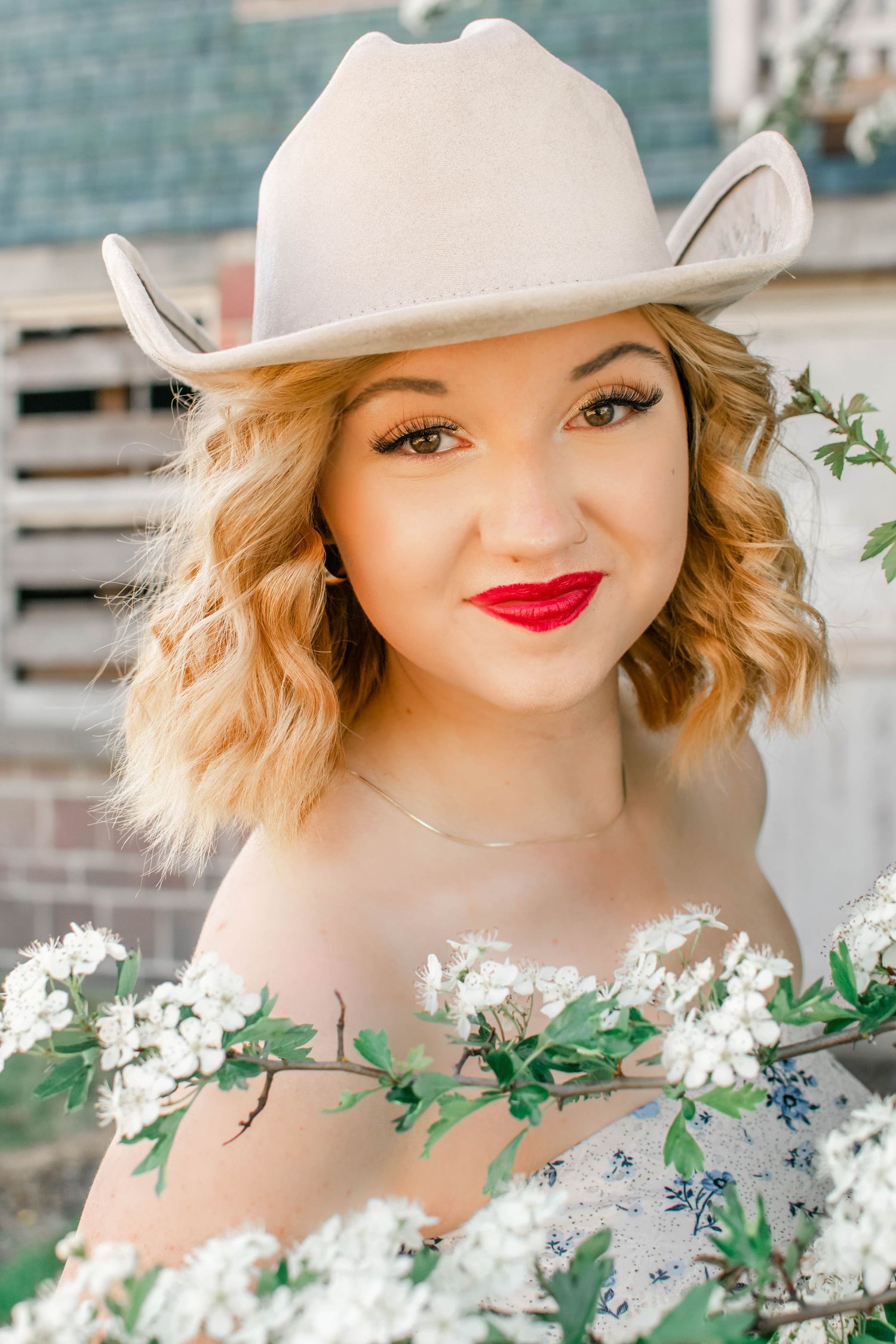 Spring fashion portrait featuring white hat, red lipstick and floral details against brick background.