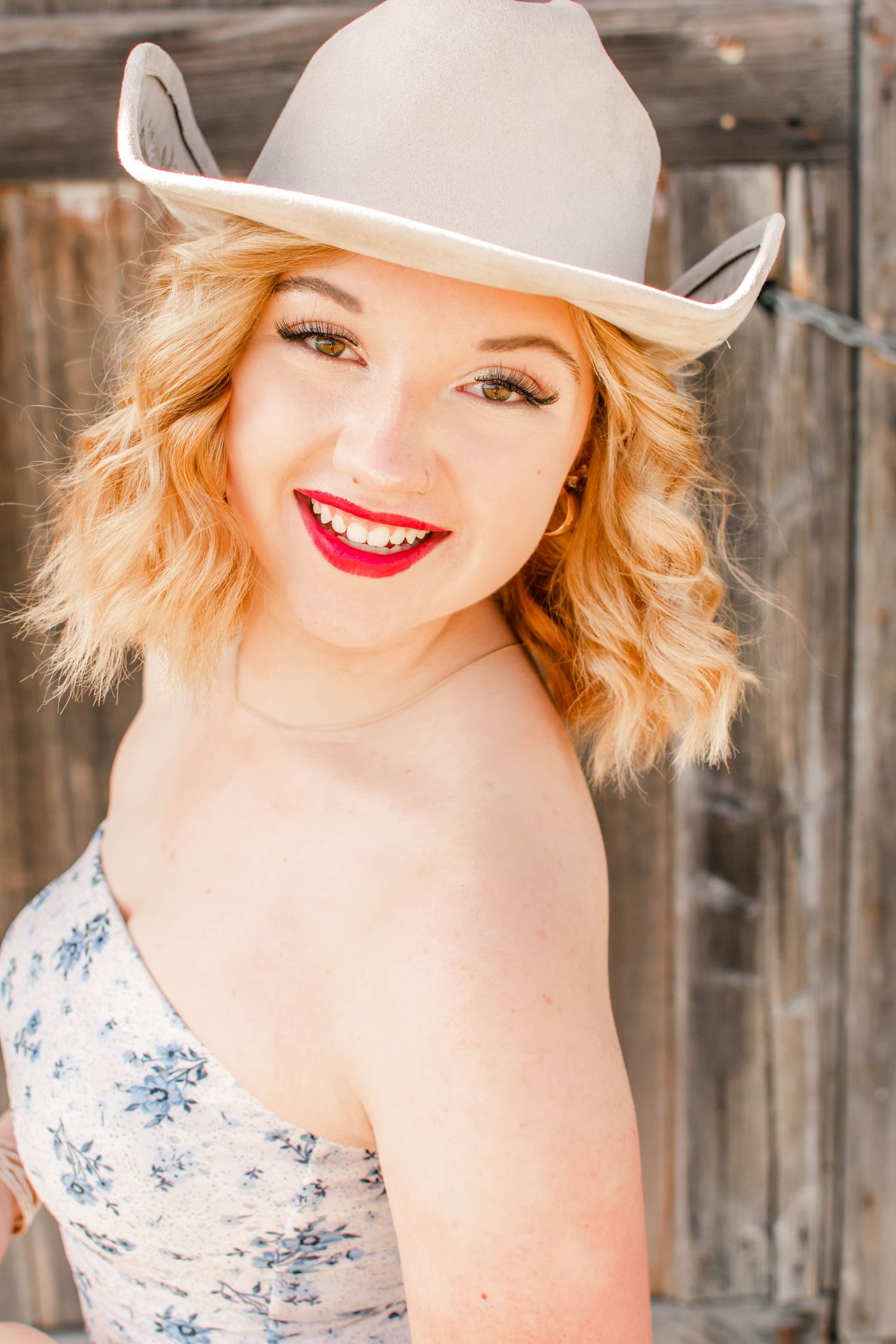 Rustic fashion portrait with white cowboy hat and floral dress against wooden background.
