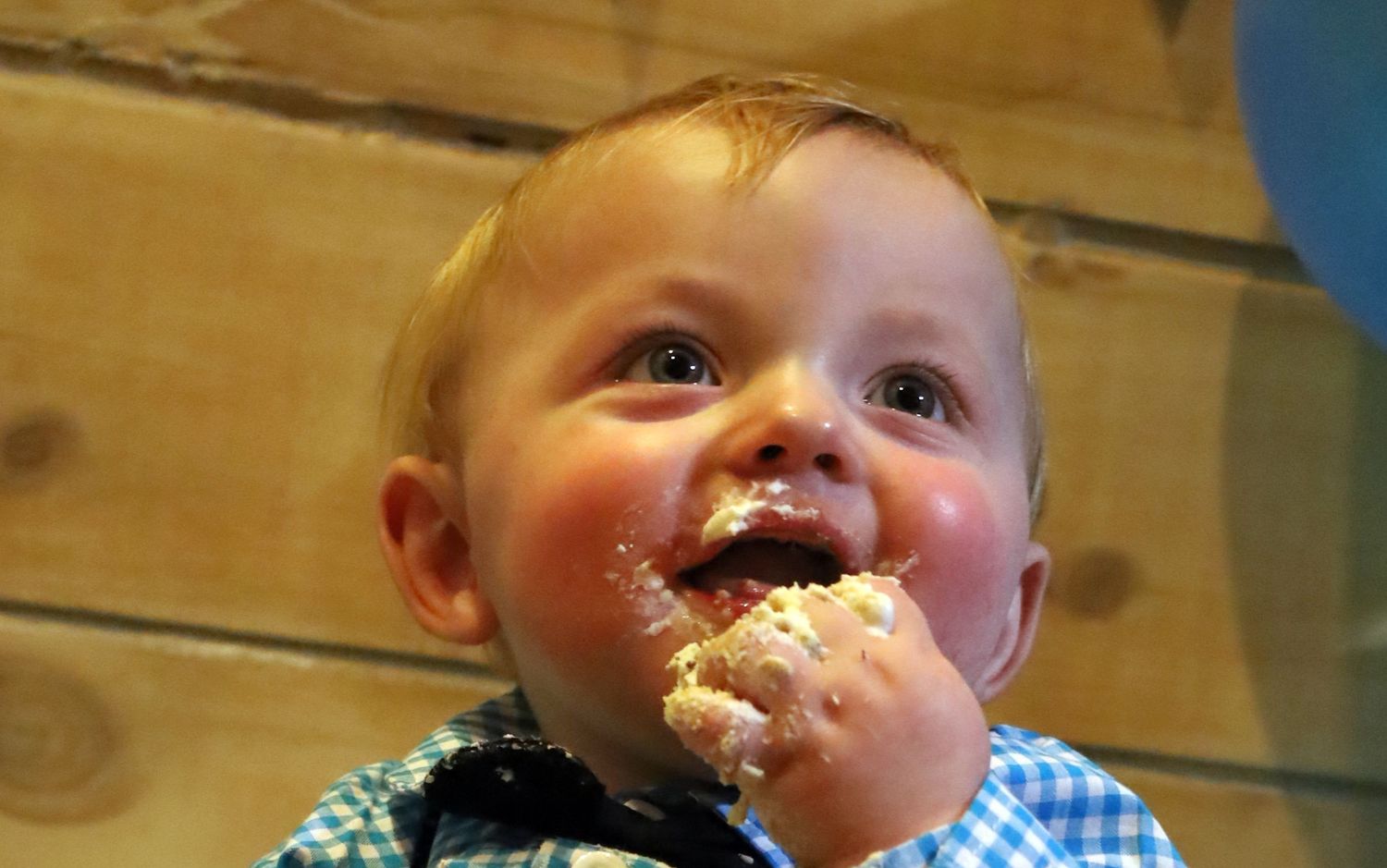 Adorable red-haired baby boy eating cake with frosting on his face during his first birthday.