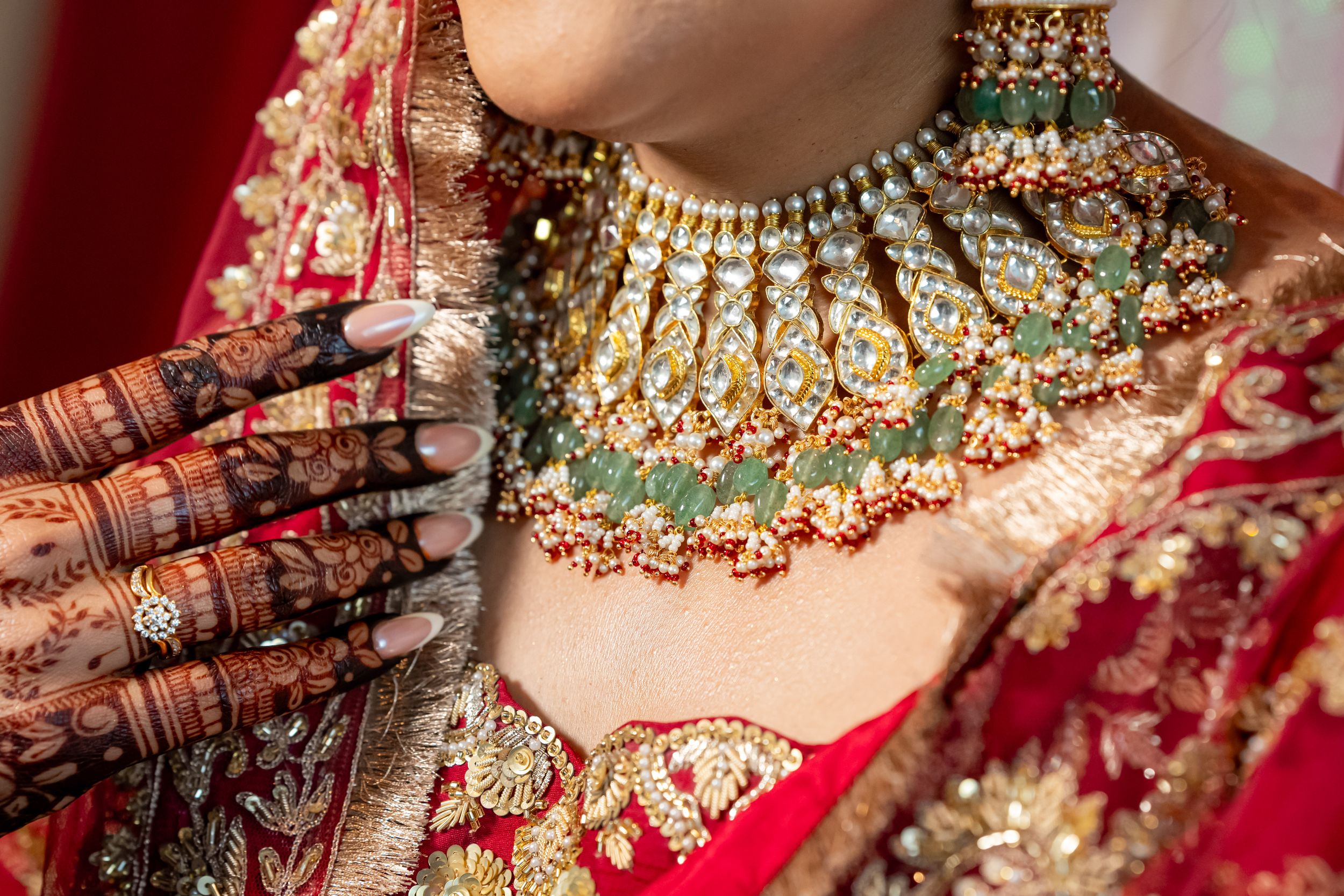Close up of traditional Indian bridal jewelry and henna adorned hands with ornate red and gold wedding attire.