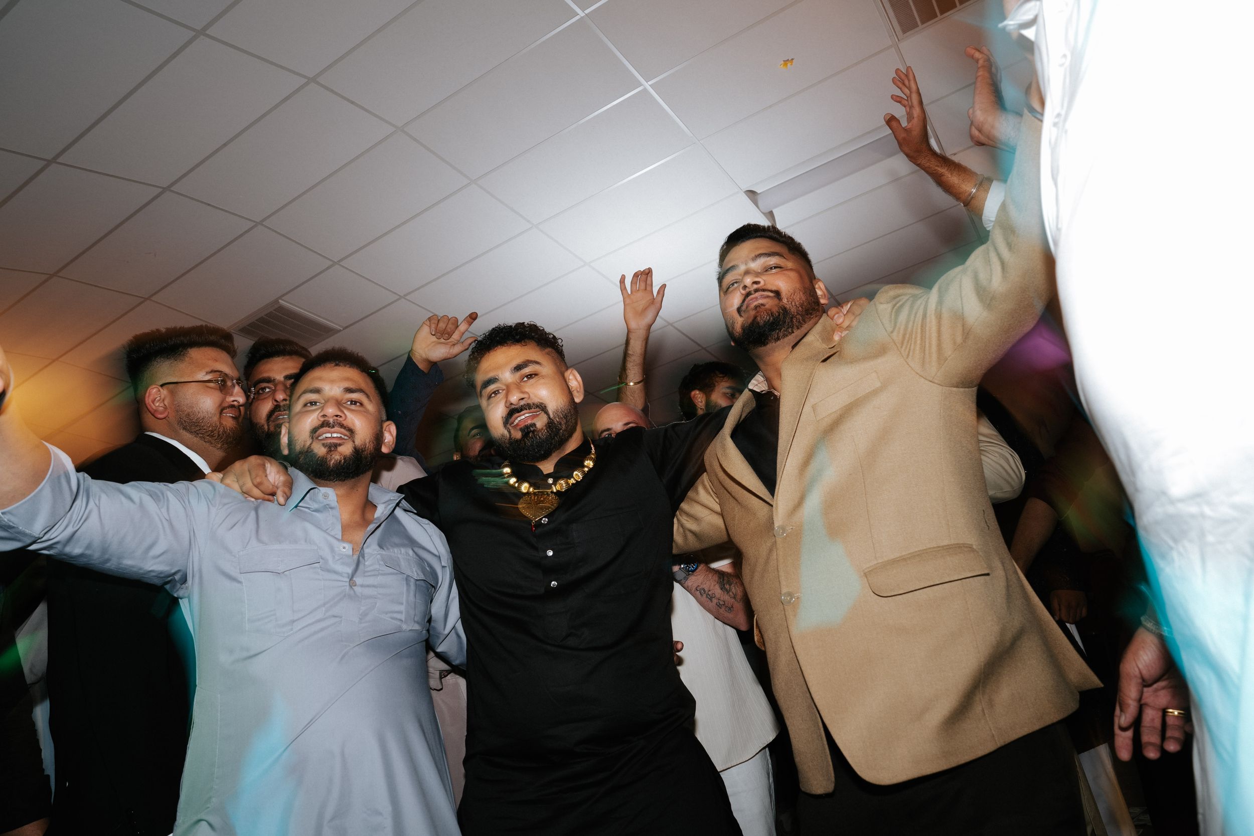 Group of men dancing and celebrating joyfully at an indoor party or wedding reception event.