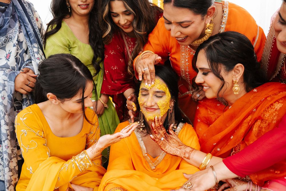 Women applying haldi turmeric paste on bride during traditional Indian Haldi ceremony celebration.
