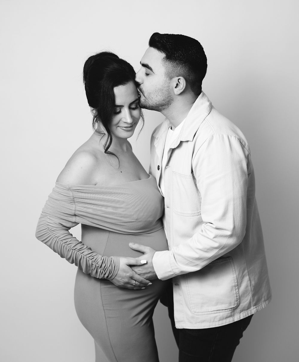 A black and white photo shows an intimate moment between an expecting couple embracing during a maternity photoshoot in London