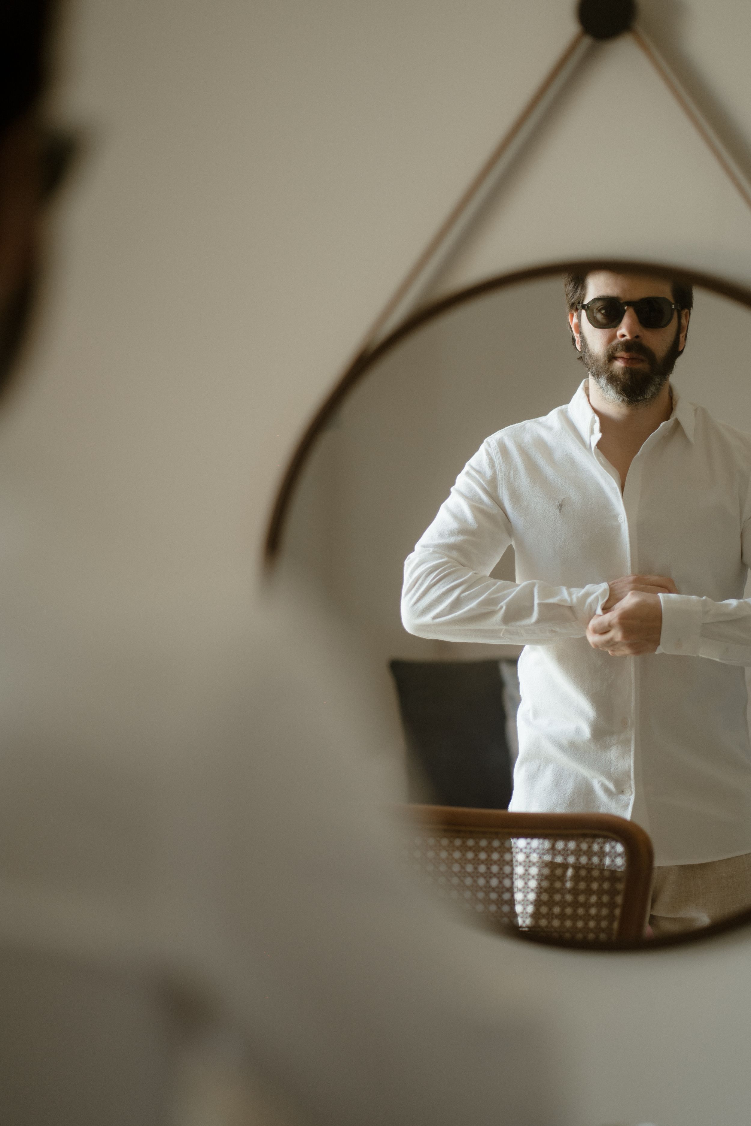 A stylish reflection in a hanging mirror shows someone buttoning a crisp white shirt.