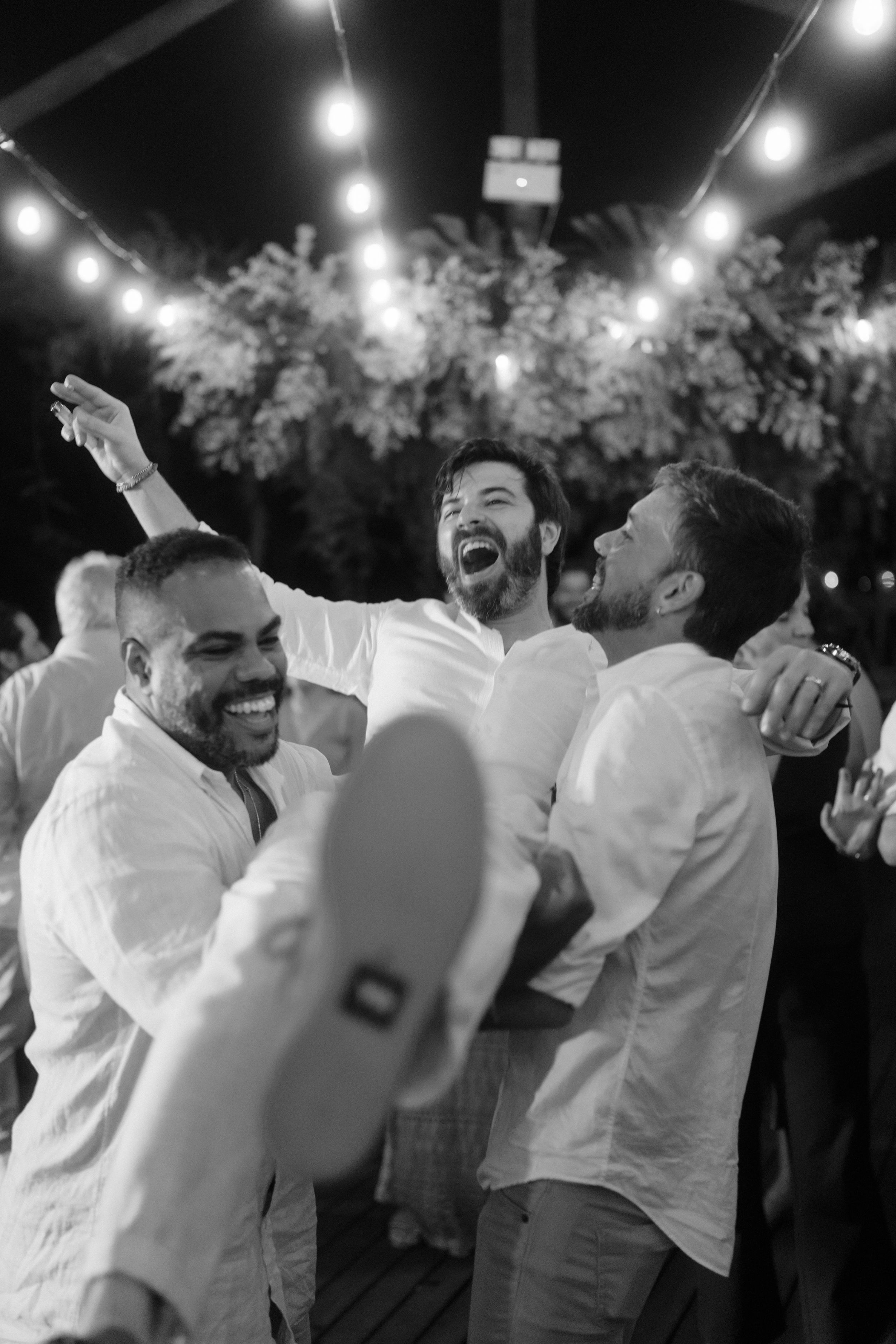 Guests in white attire dancing and celebrating together under outdoor string lights at night.
