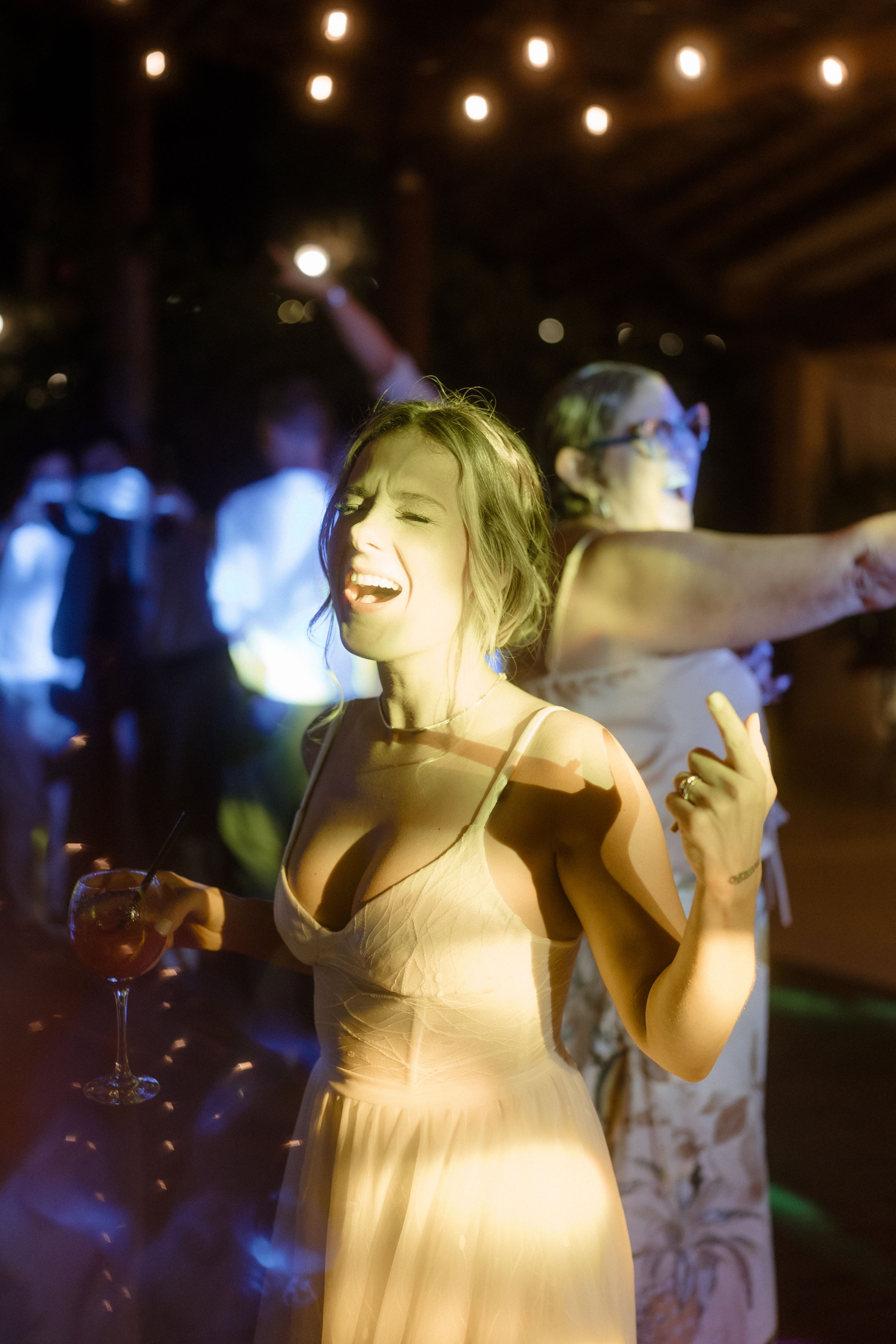 Performer in light dress singing passionately on stage under dramatic lighting at evening event.