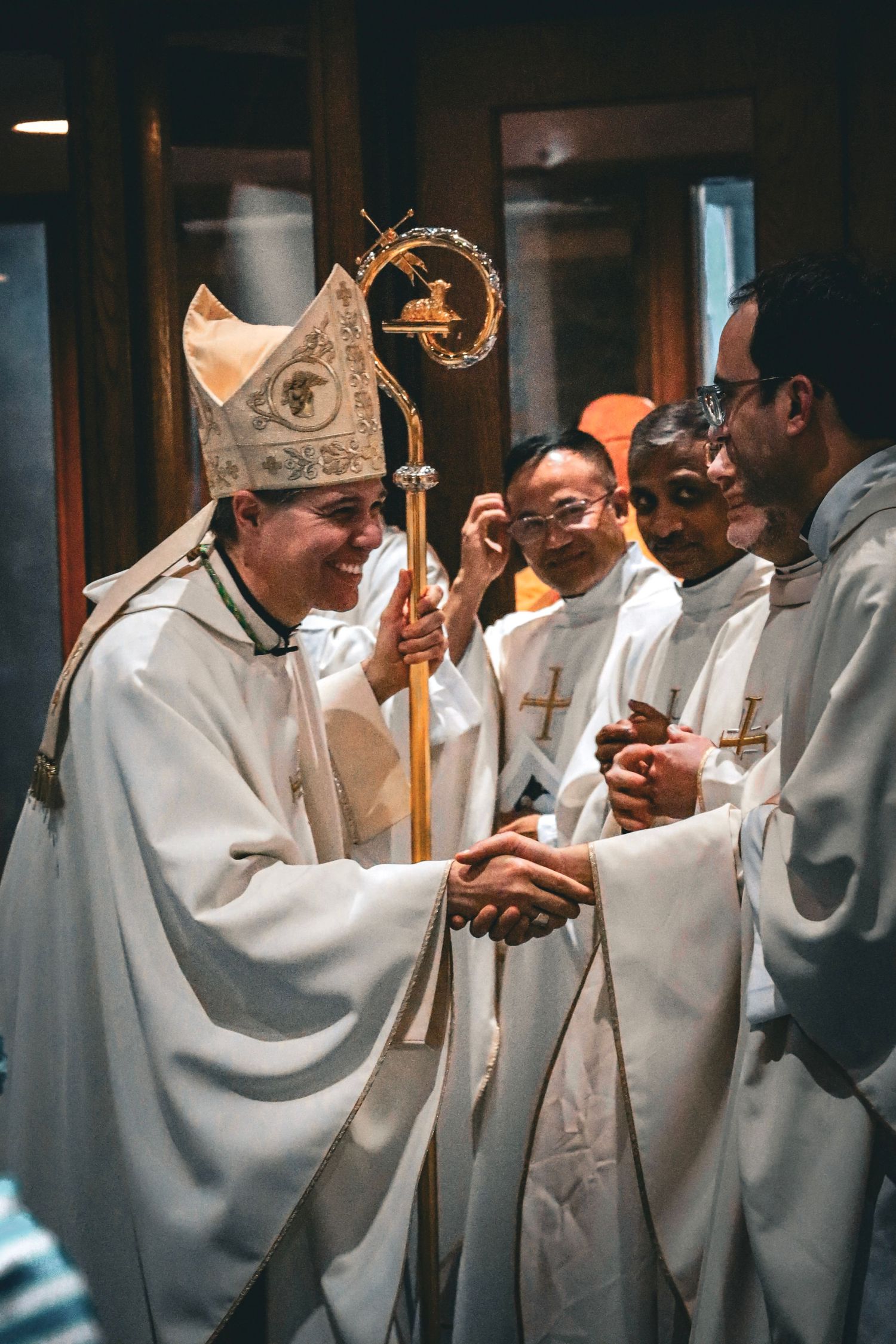 A religious ceremony shows clergy in white robes and a bishop with traditional mitre and staff greeting others.