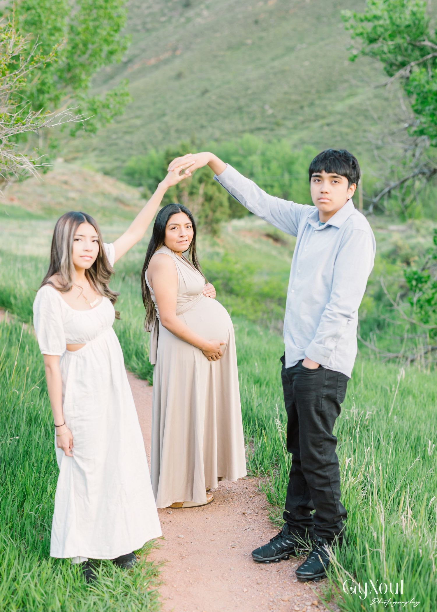 A group poses together on a hiking trail with two women in flowy dresses and someone holding up their arm in an arch.