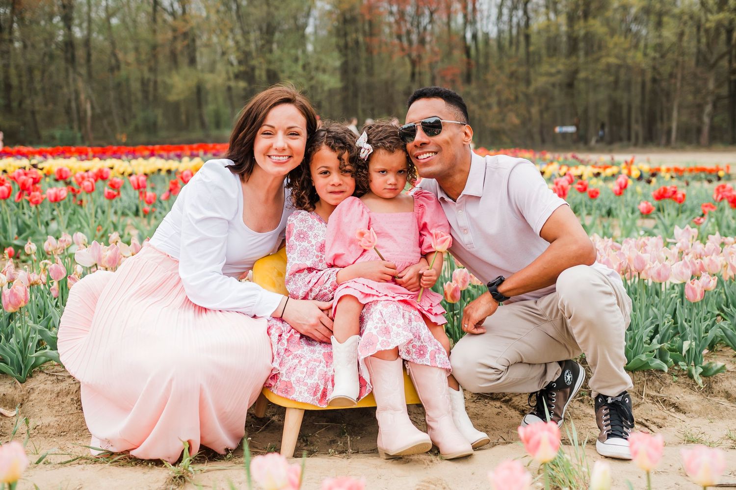 A family poses together in a colorful tulip garden during spring, wearing coordinated pink and white outfits.