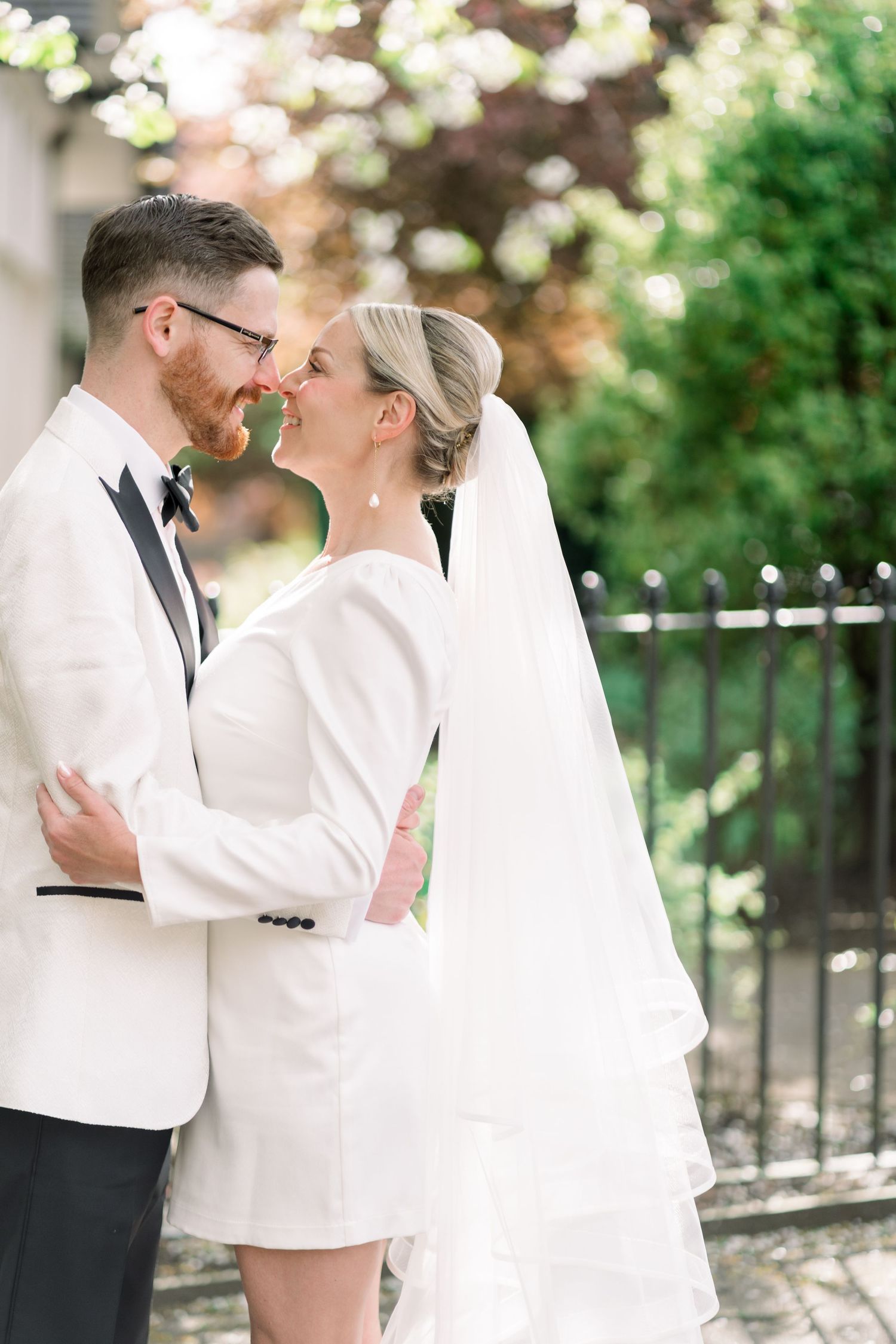 Bride and groom lovingly smile at each other, embraced behind greenery with a spring-summer glow in The Park, Nottingham city elopement.