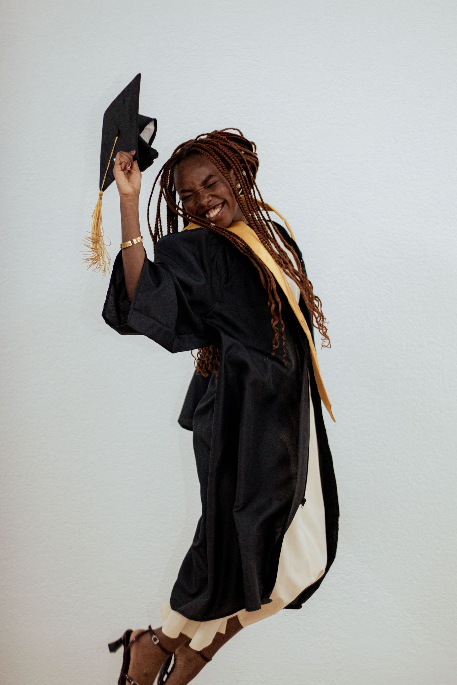 Graduate student wearing black graduation gown and cap jumps joyfully while celebrating their academic achievement.