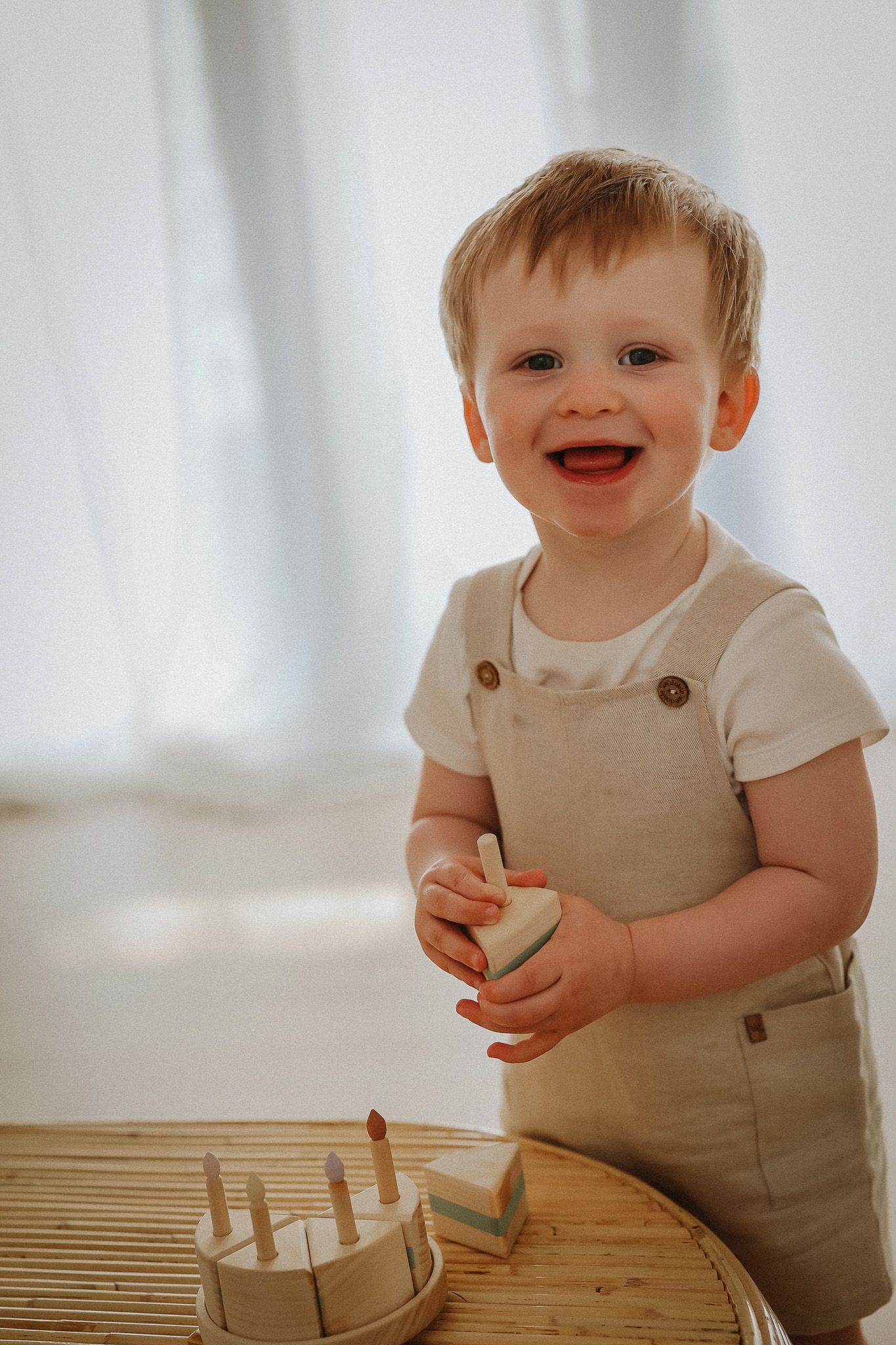 Baby in white shirt sits on plush rocking horse toy against cream-colored background.