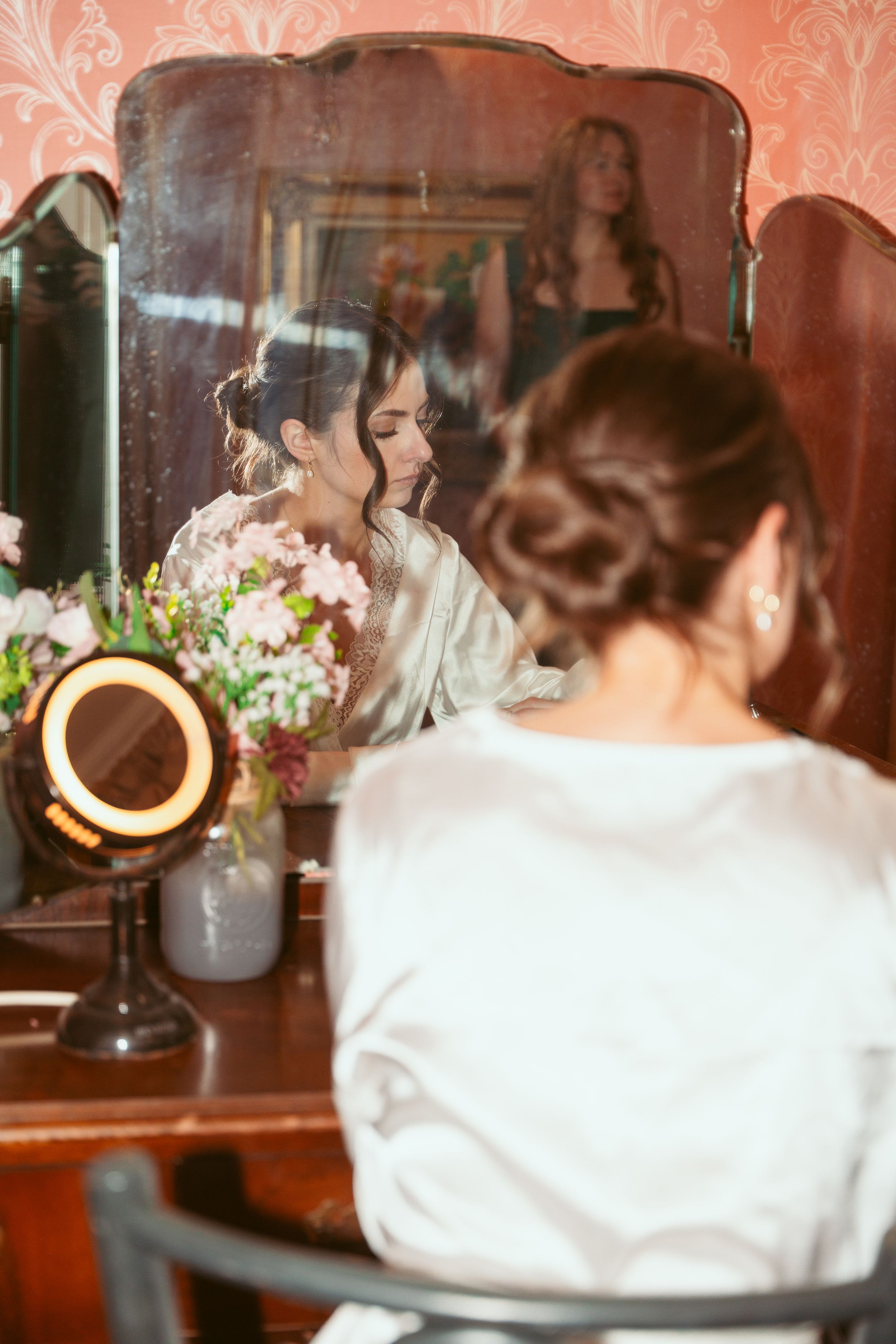 Elegant bridal preparation scene with white robe and vintage vanity mirror adorned with delicate floral arrangements.