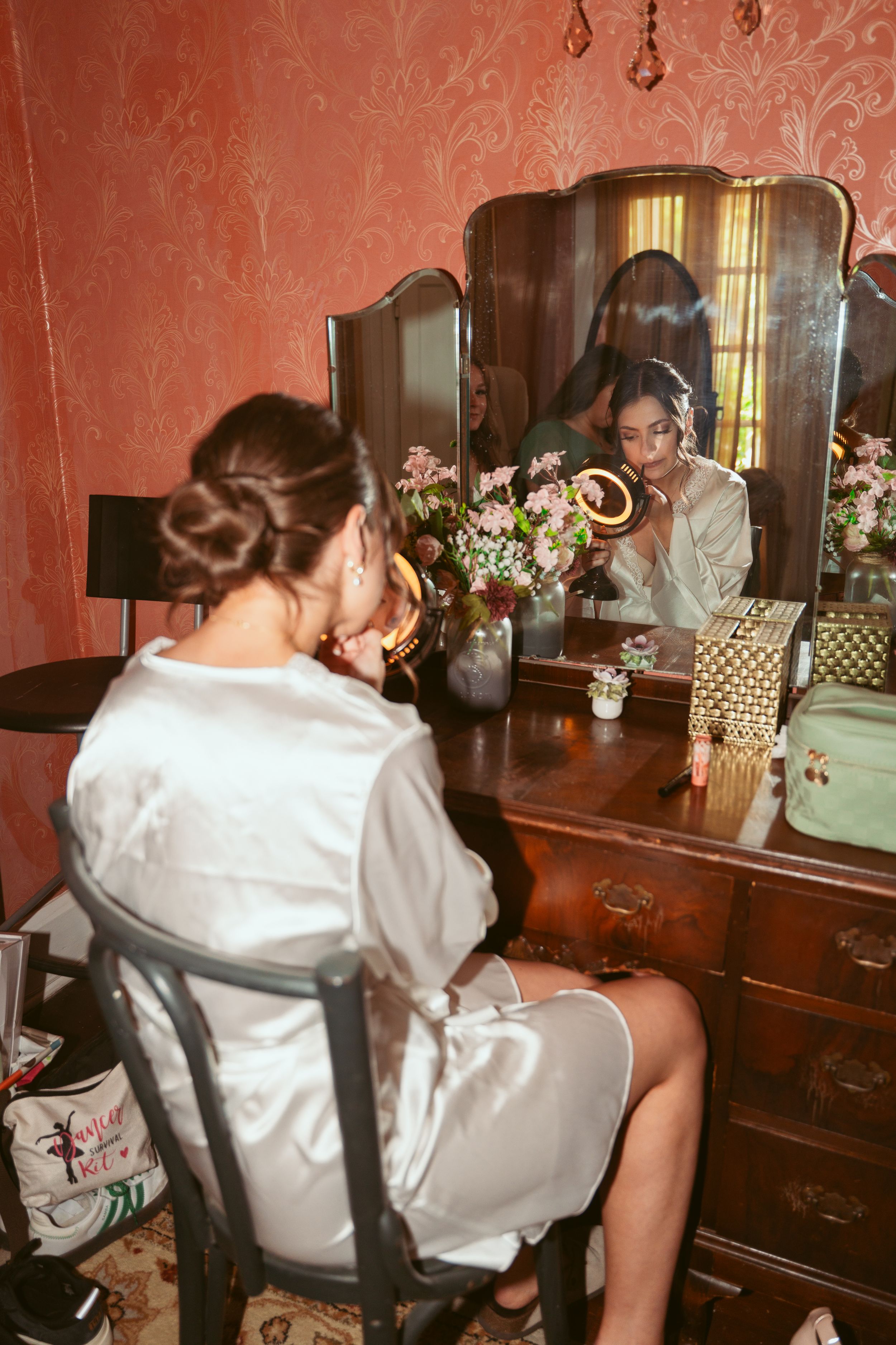 A behind-the-scenes wedding preparation moment at an antique vanity with mirror reflections and flowers.