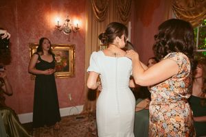 A candid moment at an elegant wedding reception with women in formal attire in a red-walled room with chandeliers.