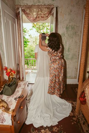 Vintage-style dresses hanging between white curtains in a romantic, rustic bedroom setting with natural lighting.