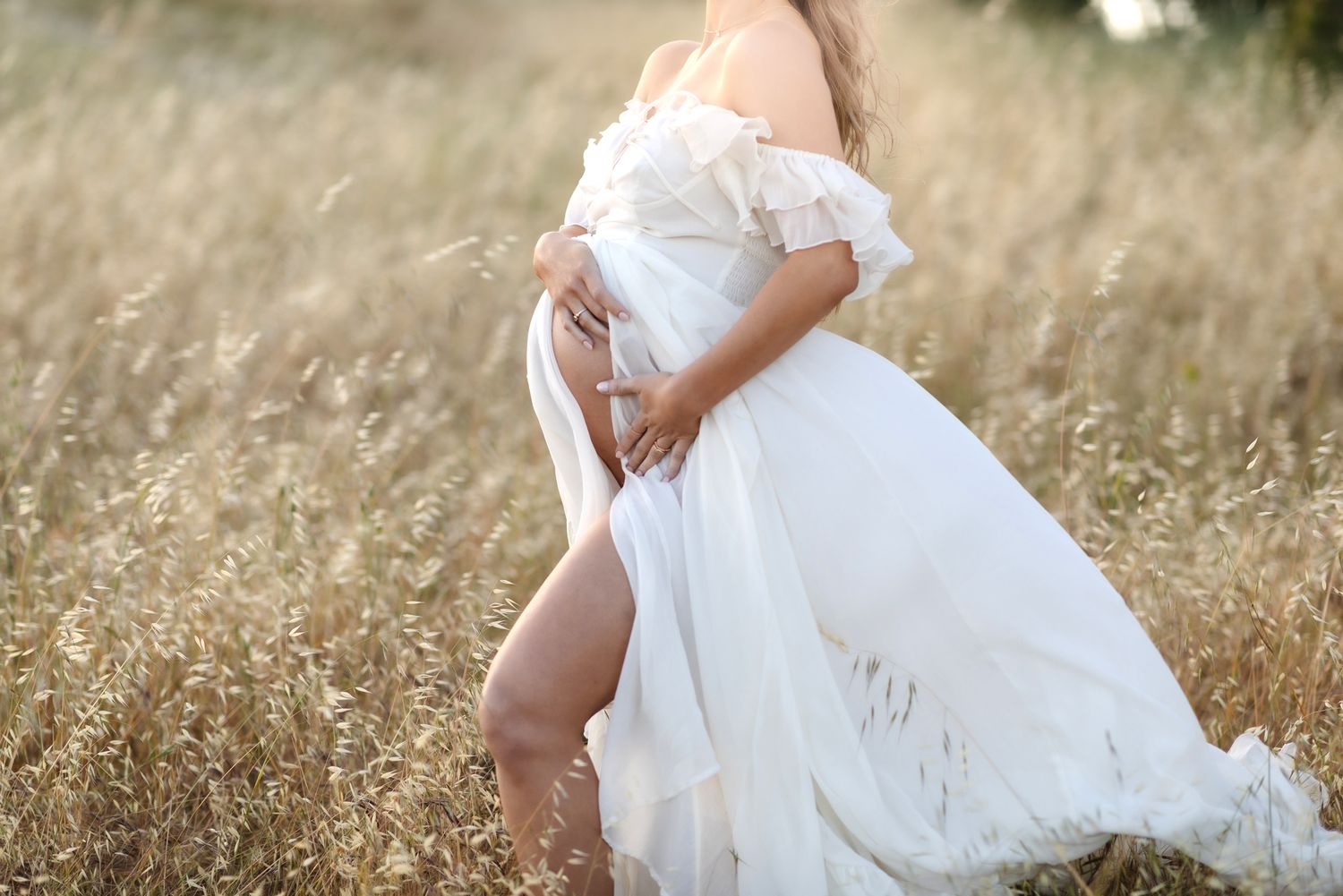 Expectant mother wears a sheer white maternity gown in grassy field. North Shore, Lakes Region Seacoast New Hampshire maternity photographer