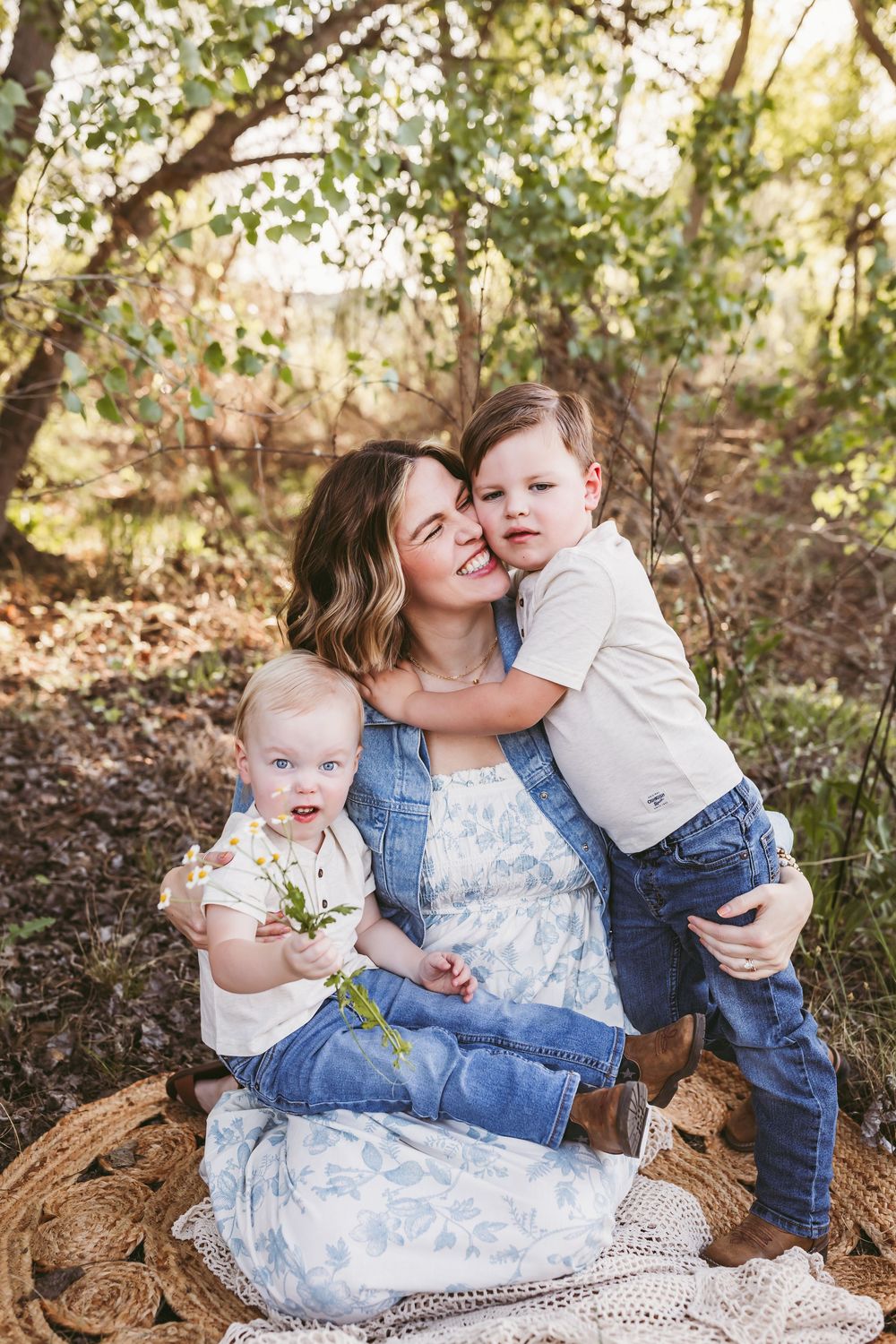 A mother sits outdoors hugging her two young children during a motherhood session with Heidi Grace Photography.