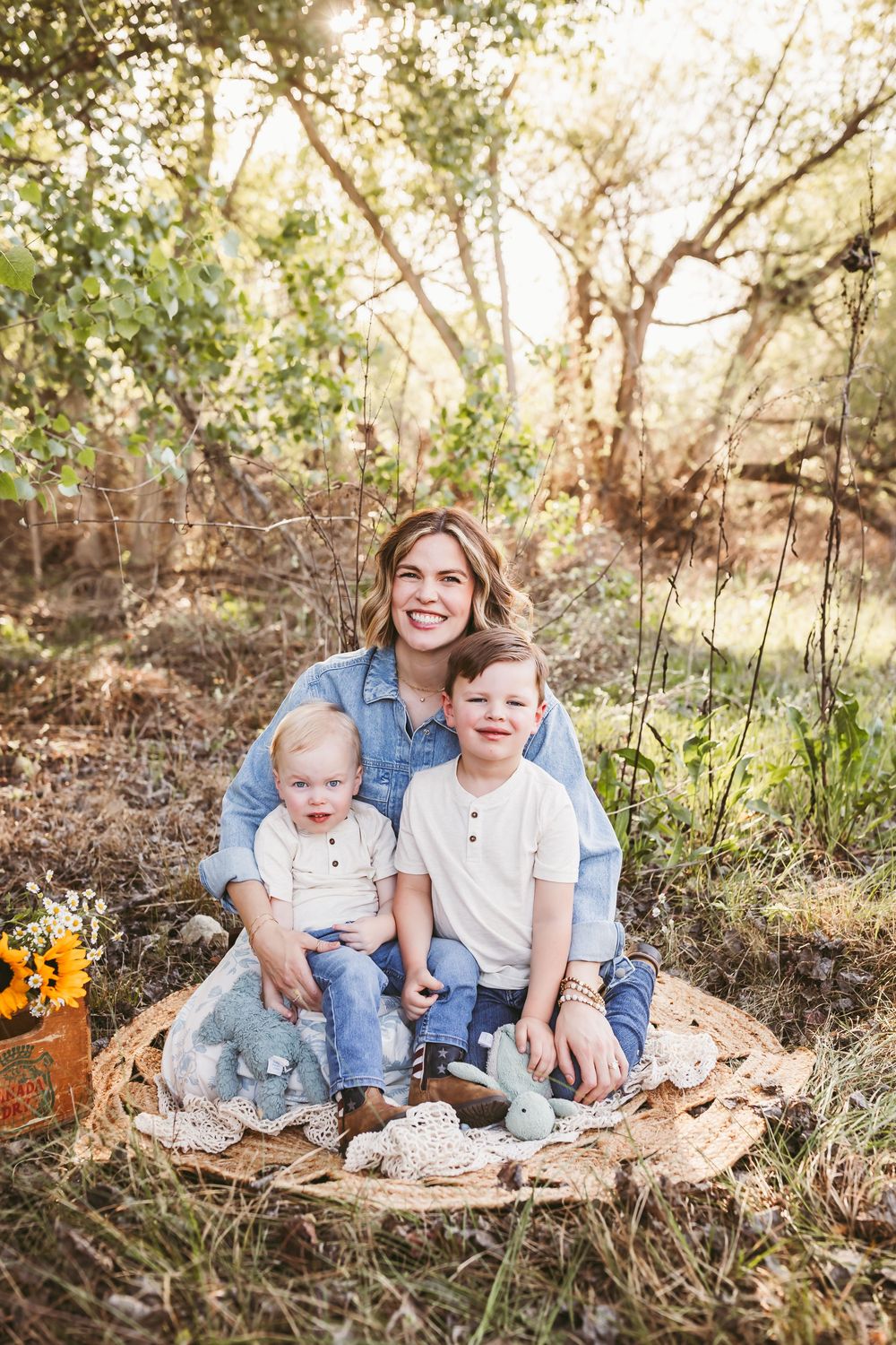A smiling mother sits outdoors in nature with her two young sons for a spring mommy and me with Beaumont photographer Heidi Grace.