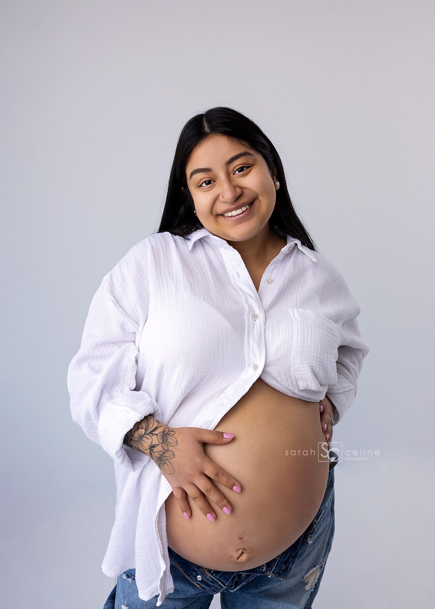 Smiling pregnant woman in white shirt and jeans cradling baby bump during maternity photo session.