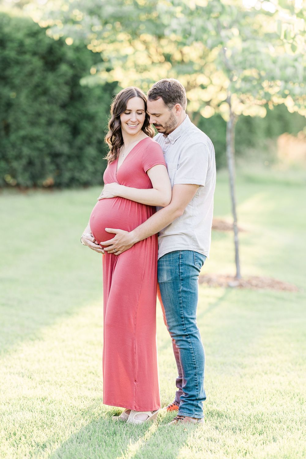 Couple sharing tender moment outdoors, man embracing pregnant woman in red maxi dress.