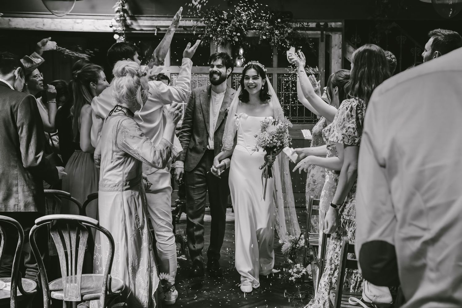 Black and white photo of a joyful couple walking through a celebratory wedding reception crowd.