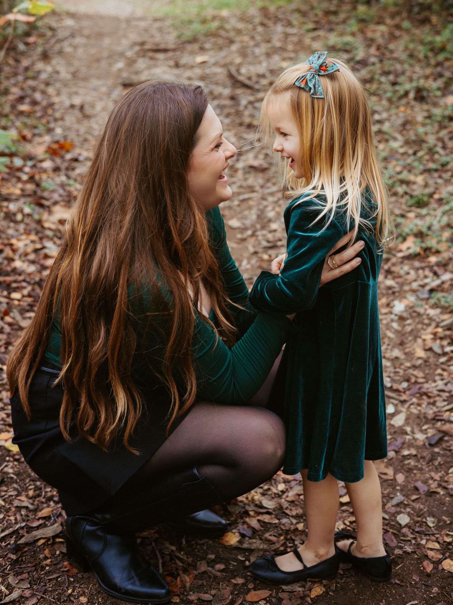 A tender motherhood lifestyle portrait of a mother crouching down to look at her young daughter during an outdoor session.