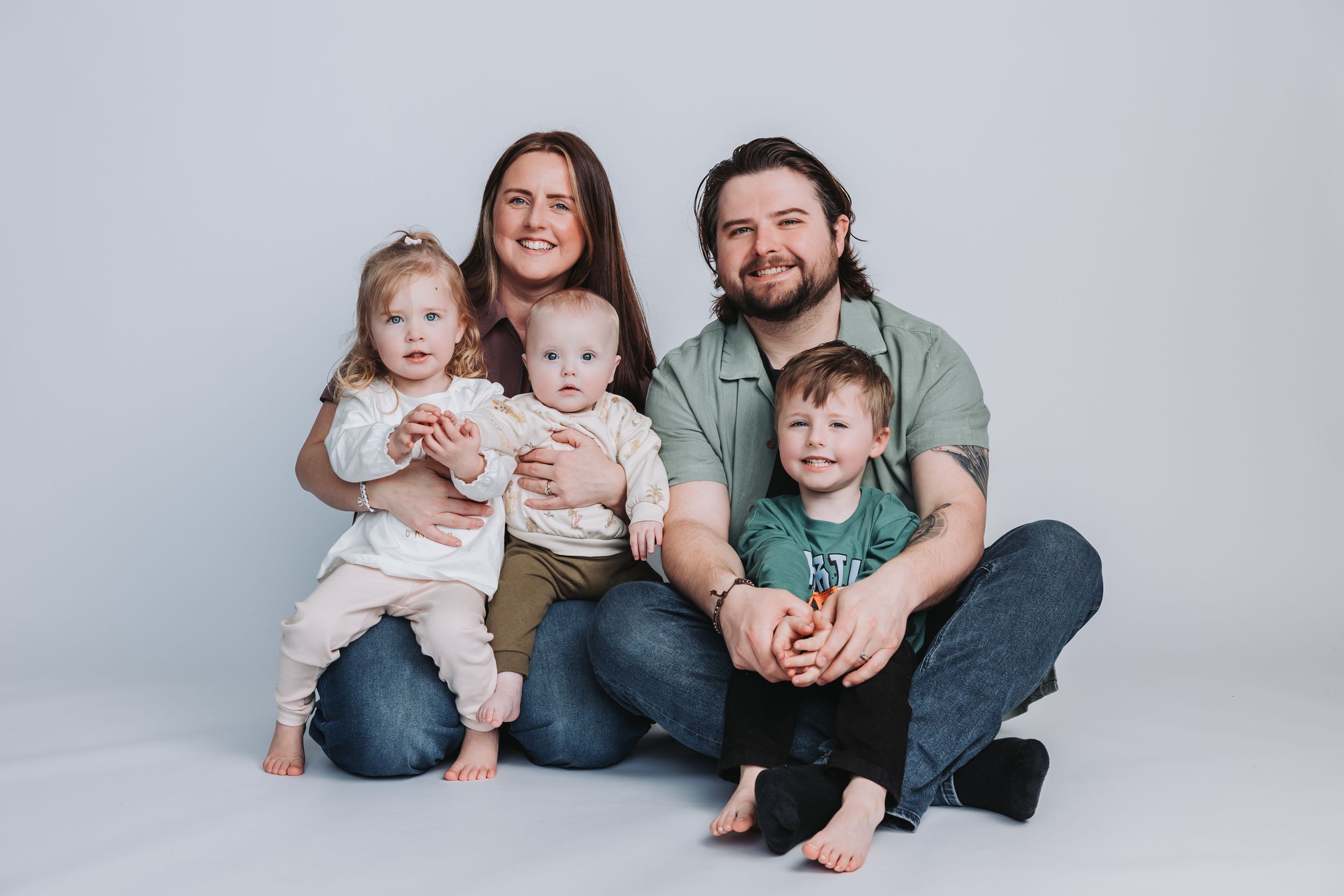 Family of five posing for a studio portrait, parents with three young children smiling against a light gray background.