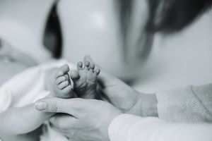 Black and white photo of a mother and father gently holding their newborn baby's tiny feet.