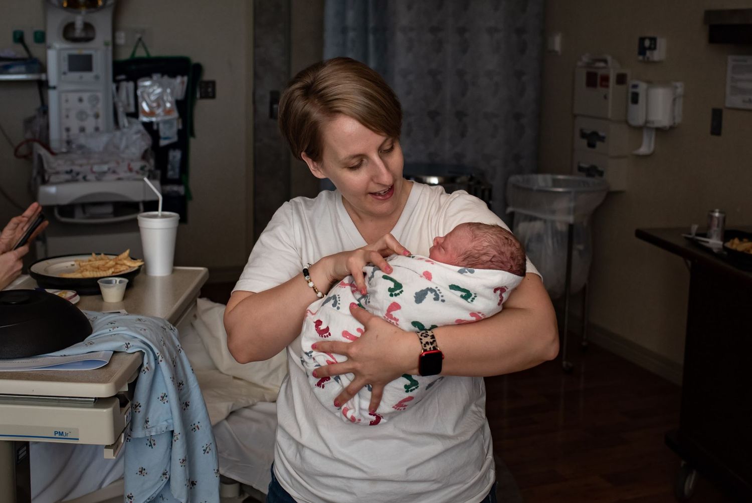 doula photographer carefully holding newborn baby wrapped in patterned swaddle blanket.
