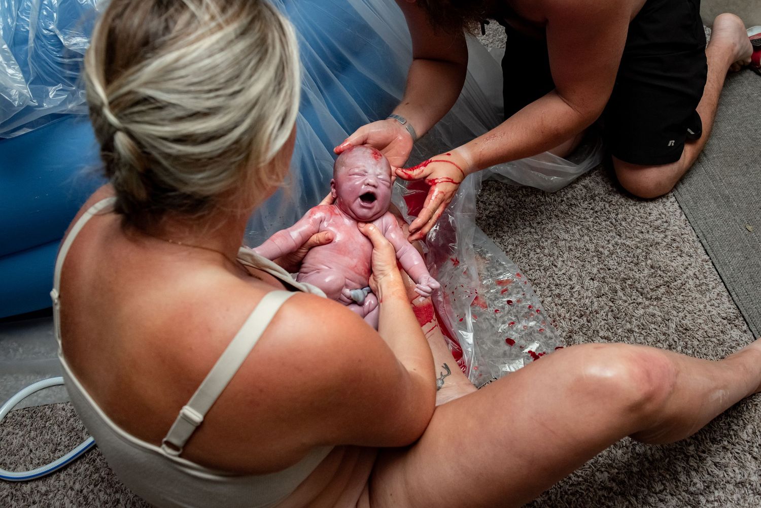 A newborn baby cries during their first moments after birth while being attended to by medical staff.