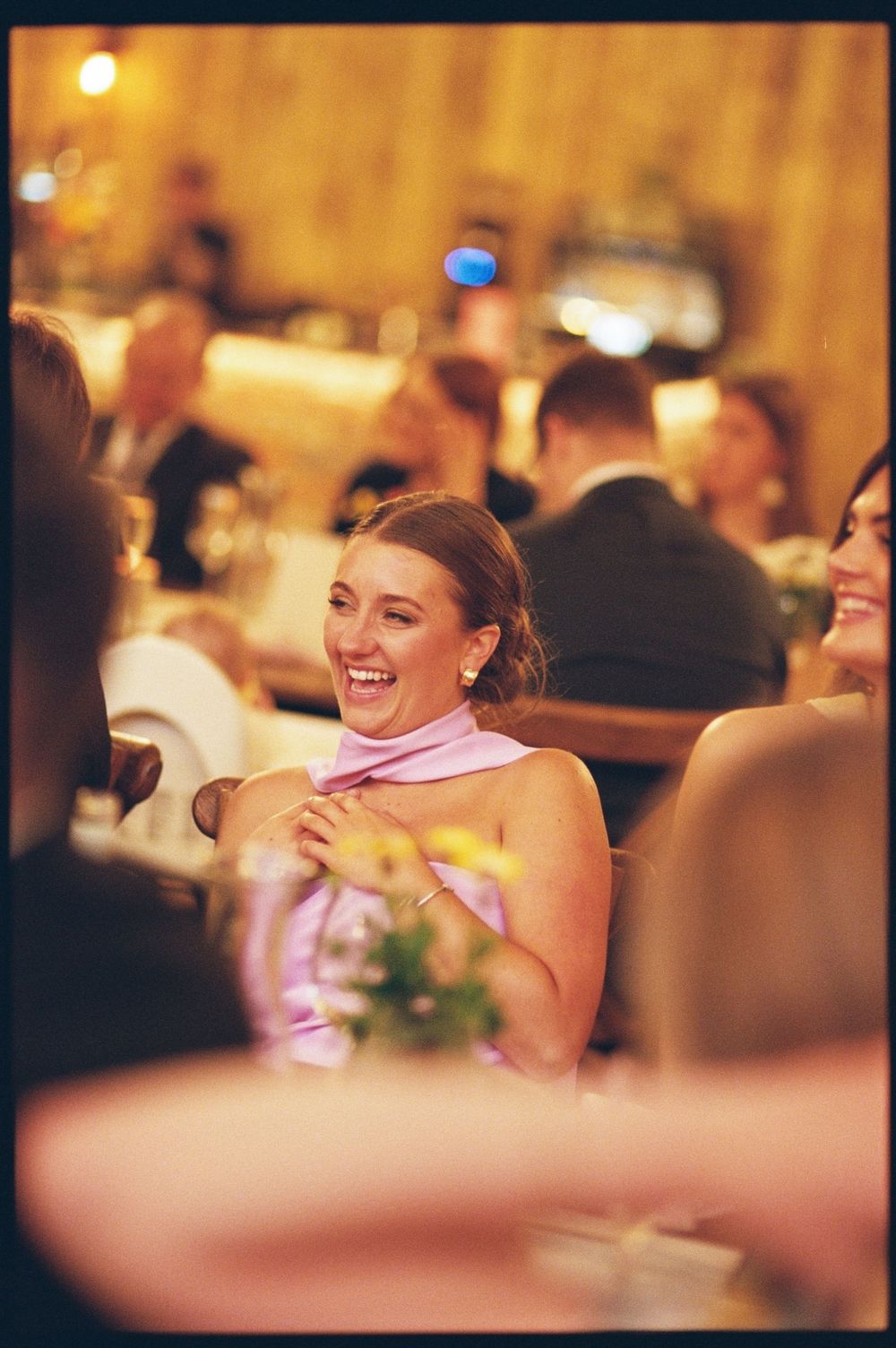 A woman in a pink dress laughs joyfully at an elegant indoor event or gala dinner.