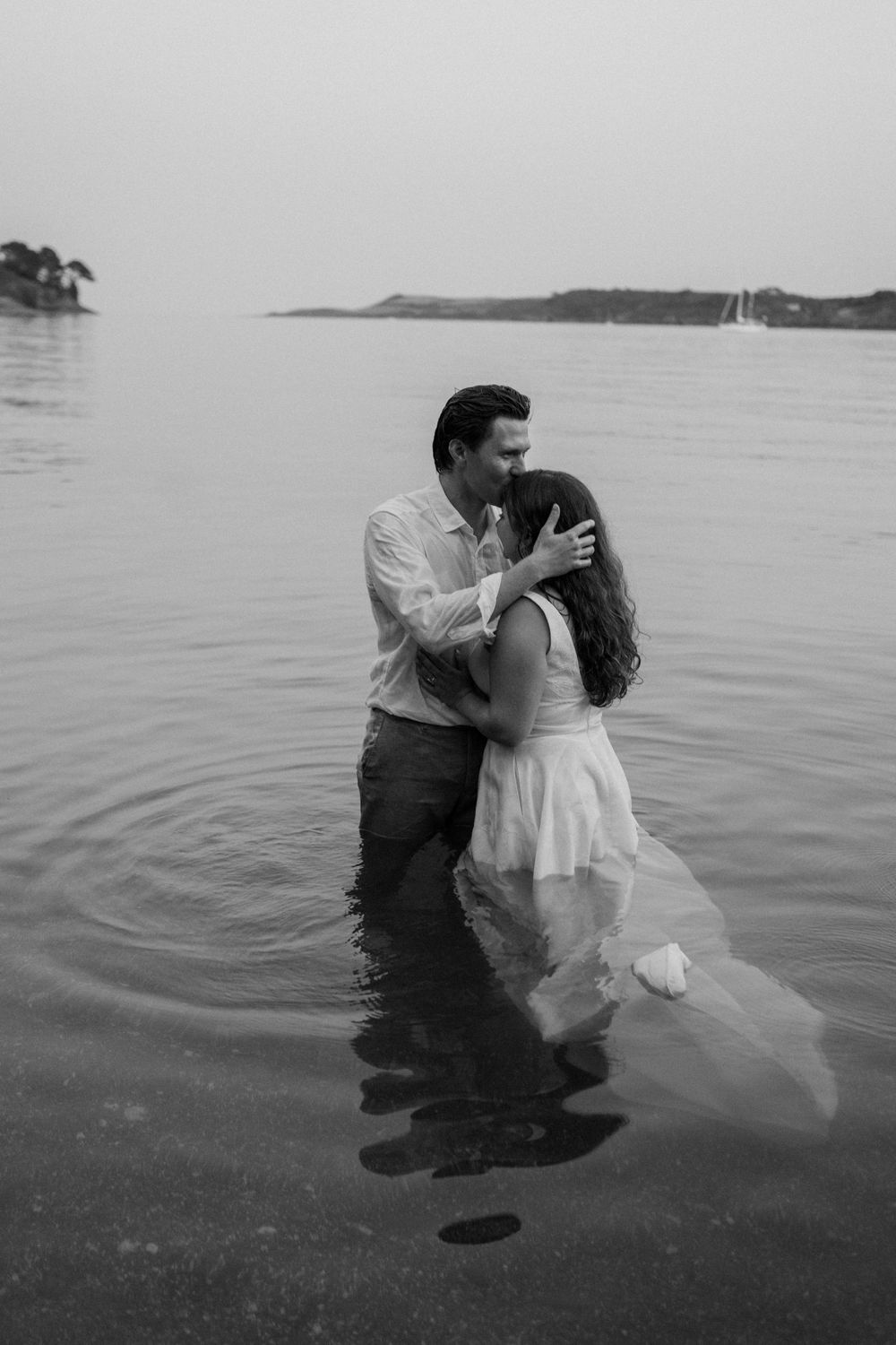Couple embracing romantically in ocean water during sunset, black and white engagement photo.