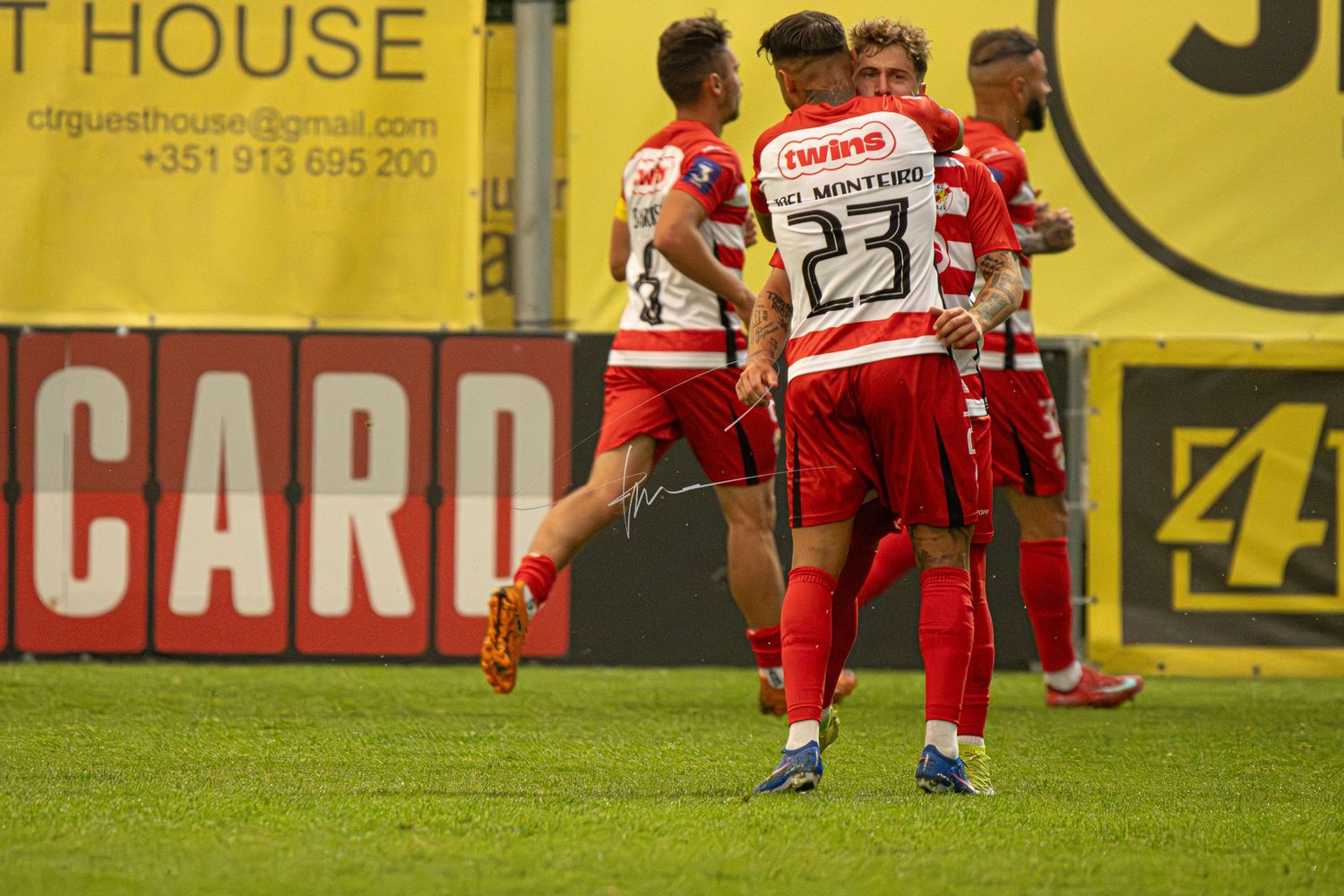 Soccer players in red uniforms celebrate a goal on the field during a competitive match near advertising boards.