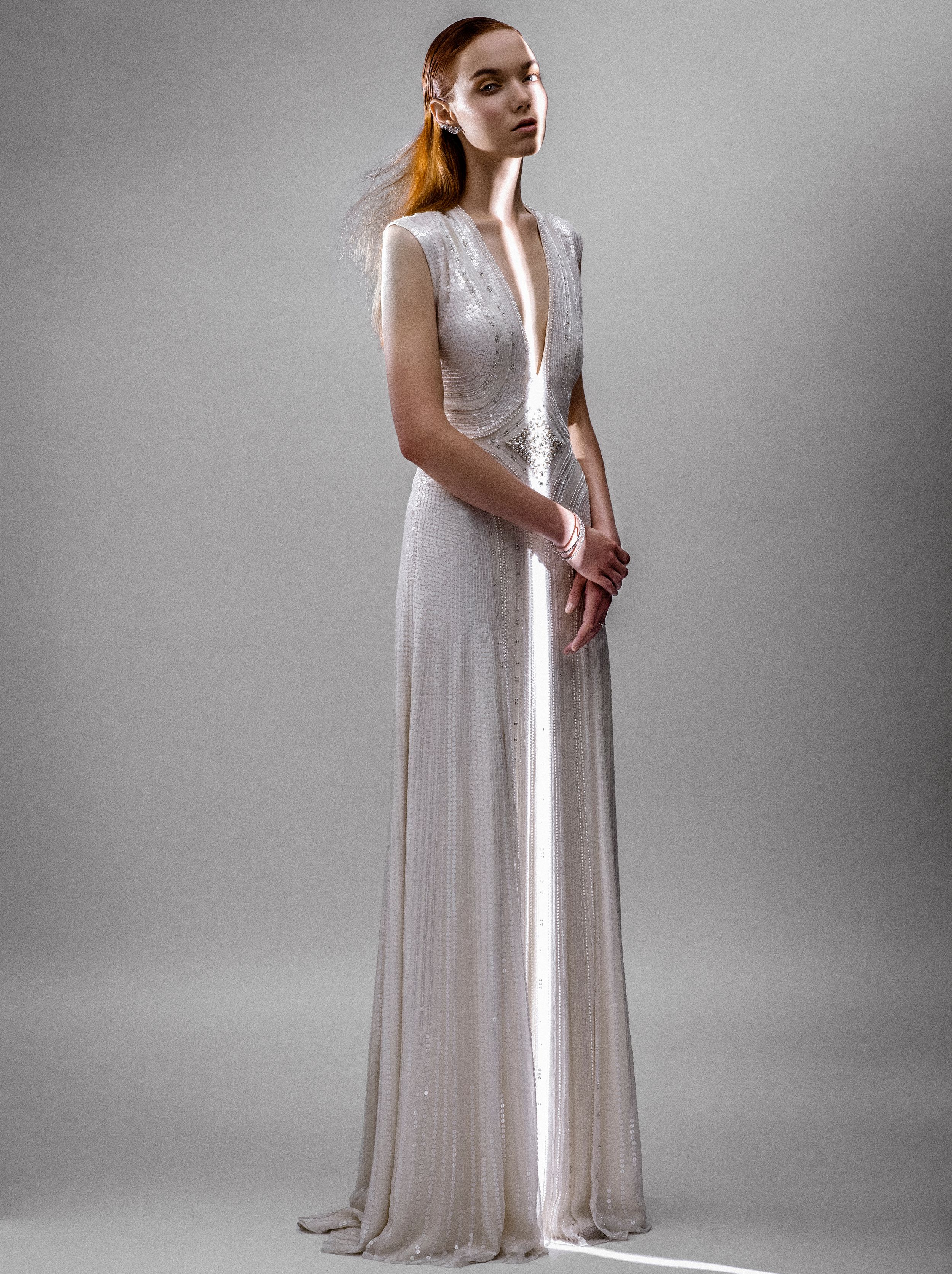 Elegant white beaded deep V-neck sleeveless bridal gown with flowing A-line silhouette on a model.