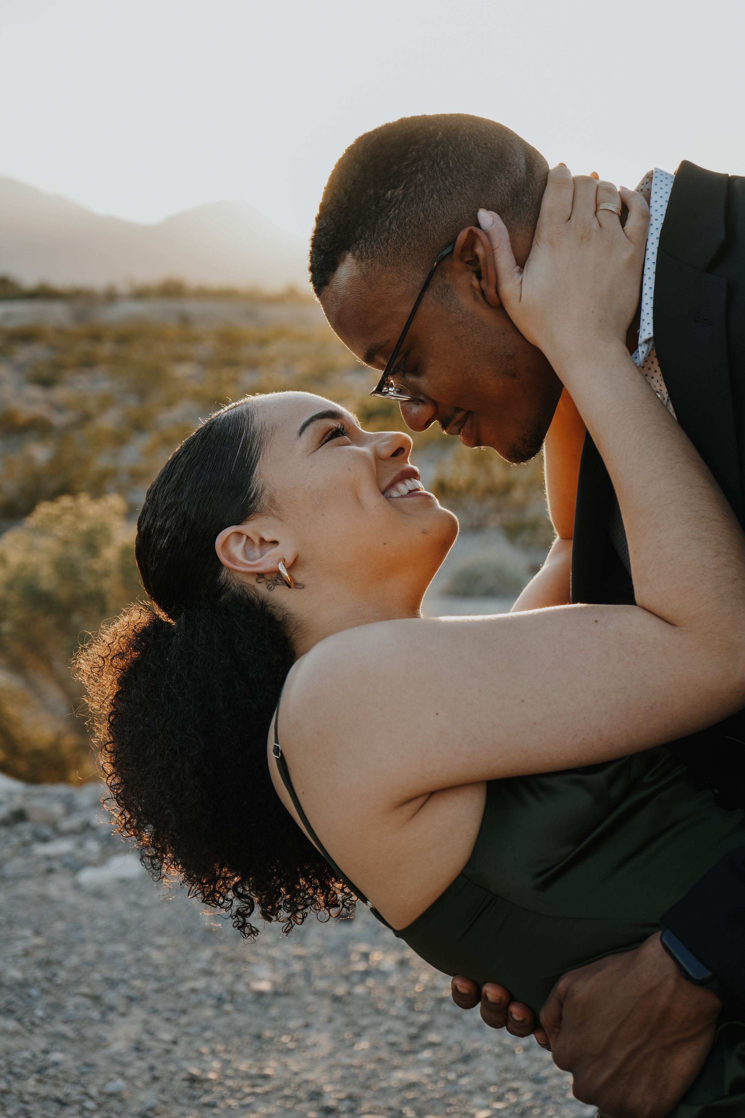 Couple sharing a romantic embrace outdoors at sunset with desert mountains in the background.