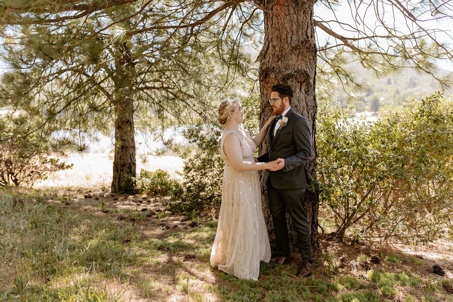 Bride and groom share a romantic moment under pine trees in a forest wedding setting at Lake Cuyamaca, Julian.