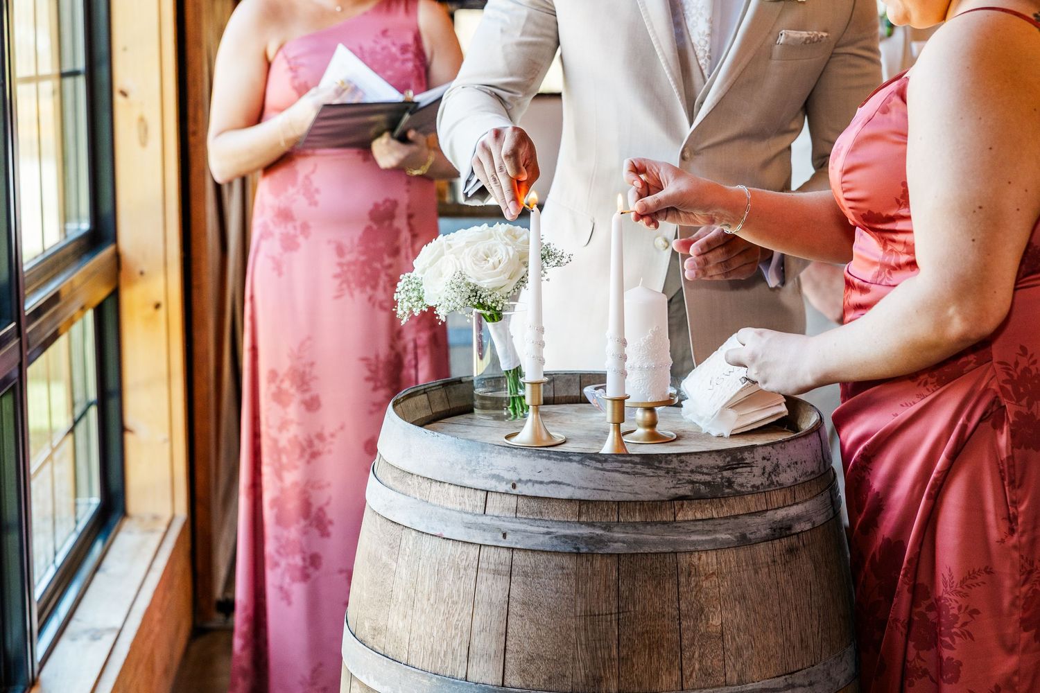 Wedding unity candle ceremony on rustic wooden barrel with bridesmaids in pink dresses.
