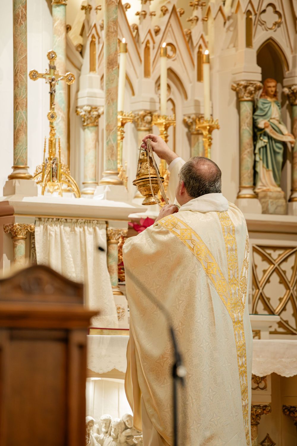 Catholic priest in ornate gold vestments performing ritual at decorated church altar during wedding Mass.