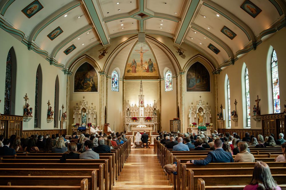 Congregation gathered inside a beautiful Catholic church with arched ceilings and stained glass windows during a wedding ceremony.