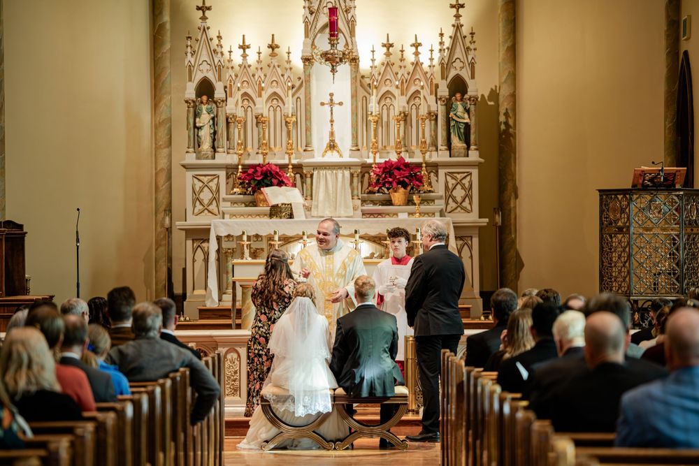 Elegant Catholic church wedding ceremony with bride and groom kneeling at ornate altar before priest.