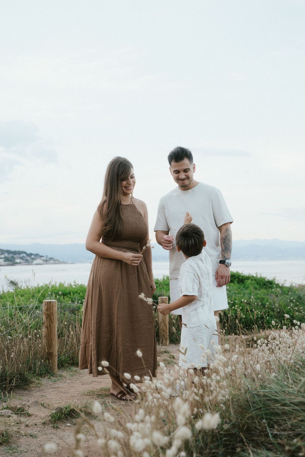 A family of three enjoys a scenic coastal path, with a pregnant woman in a brown dress, a man, and a young boy.