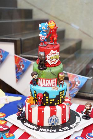 A multi-tiered Marvel Avengers birthday cake decorated with superhero figures and city skyline.