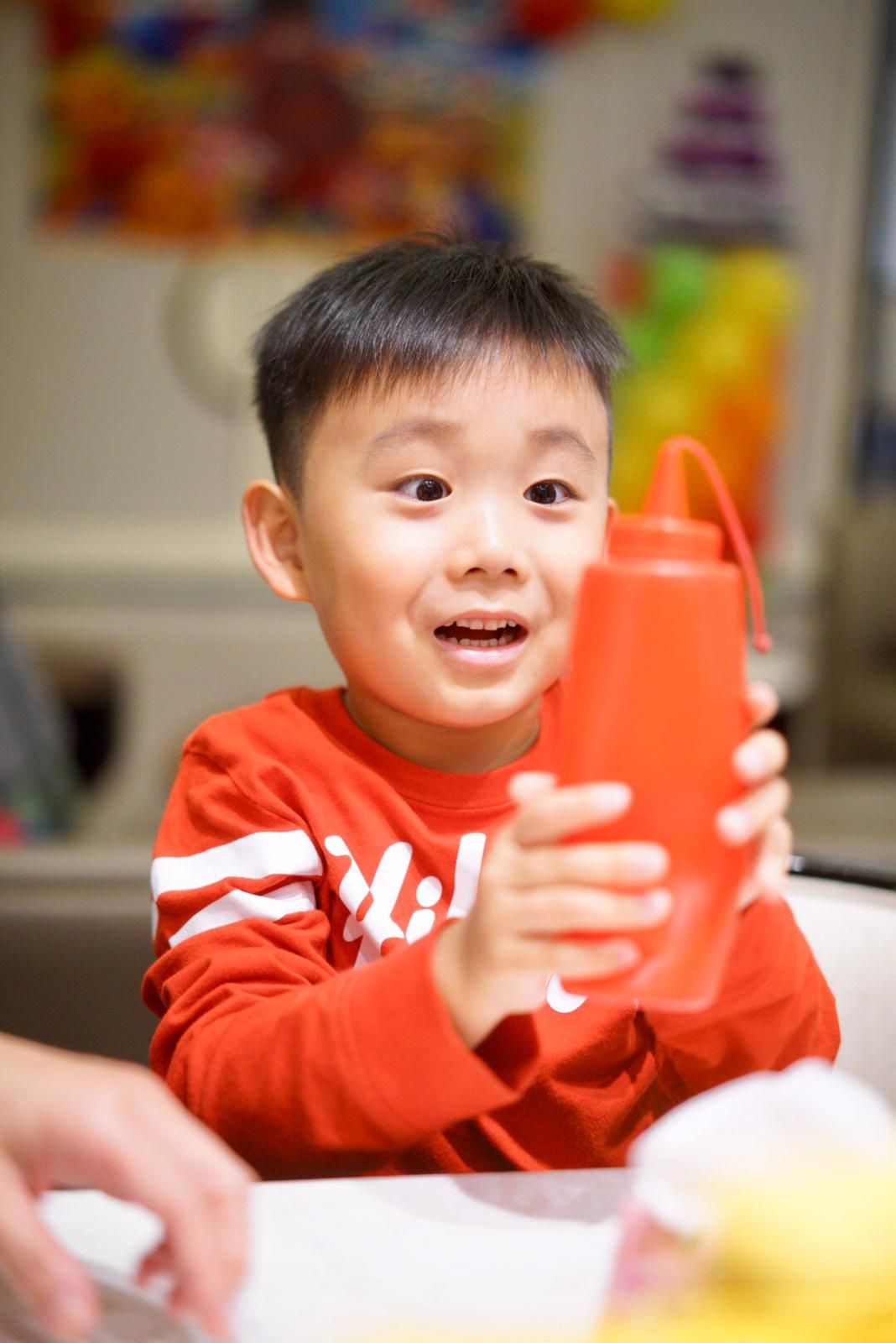 A child in a red sweatshirt holds an orange water bottle with excitement.