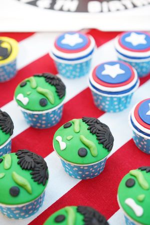 Superhero themed cupcakes featuring Hulk and Captain America designs in blue polka dot wrappers.