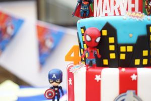 A Marvel themed birthday cake with cityscape design and superhero figurines on top.