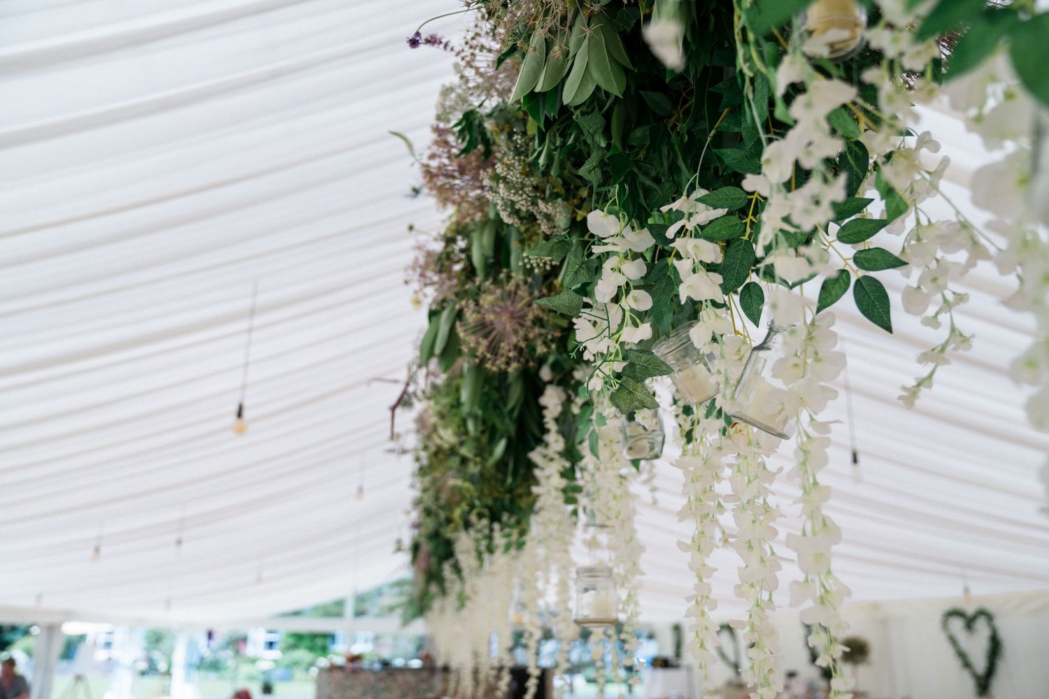 Elegant wedding marquee ceiling adorned with cascading white wisteria and lush green foliage floral installation.