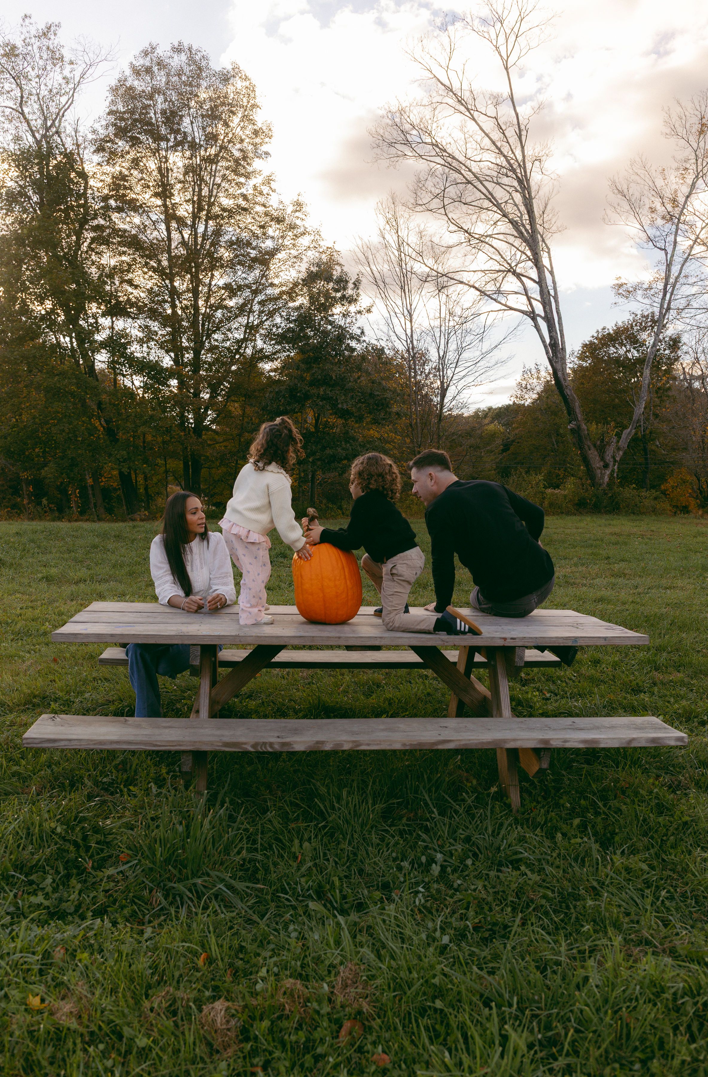 Family of four gathered around a rustic picnic table with a pumpkin outdoors in autumn.
